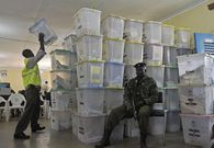 A poll official stacks ballot boxes that have been tallied on March 5, 2013 next to an armed security officer standing guard over the results at a tallying centre in Kakamega, western Kenya, a day after the country held national elections. (Photo by TONY KARUMBA/AFP via Getty Images)