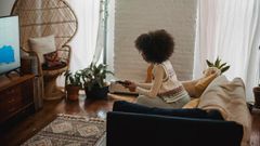 Focused young ethnic person with remote controller watching TV at home [Image credit: Andres Ayrton]