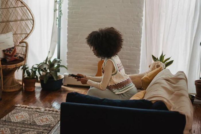 Focused young ethnic person with remote controller watching TV at home [Image credit: Andres Ayrton]