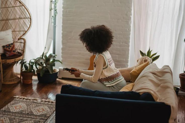 Focused young ethnic person with remote controller watching TV at home [Image credit: Andres Ayrton]