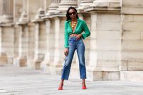 Milie Joseph wears black sunglasses, diamond earrings, a V-neck emerald green crop top with knot, a yellow shellfish necklace with multicolors stones, high-waisted mom jeans (Photo by Edward Berthelot/Getty Images)